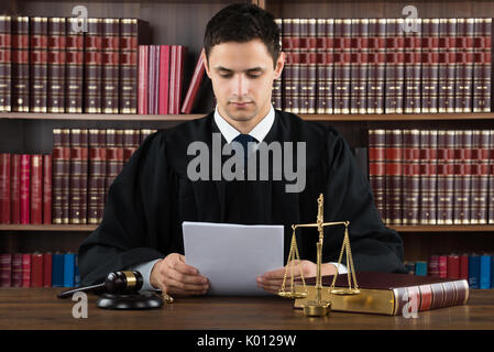 Male judge reading documents while sitting at desk in courtroom Stock Photo