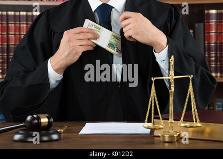 Midsection of corrupt judge putting dollar bundle in pocket at courtroom Stock Photo