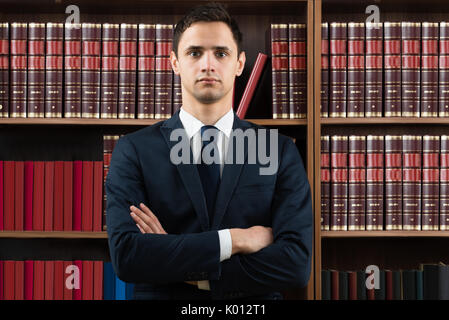 Portrait of confident male lawyer standing arms crossed against bookshelf in courtroom Stock Photo