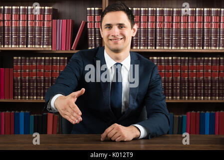 Portrait of smiling lawyer offering handshake while sitting at desk in courtroom Stock Photo