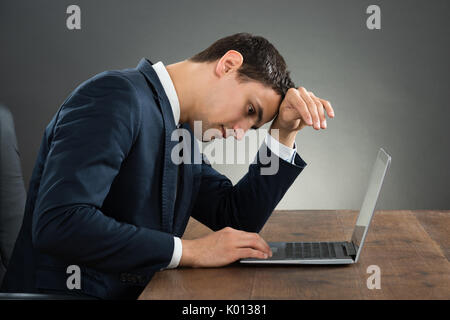 Stressed businessman using laptop at desk against gray background Stock Photo