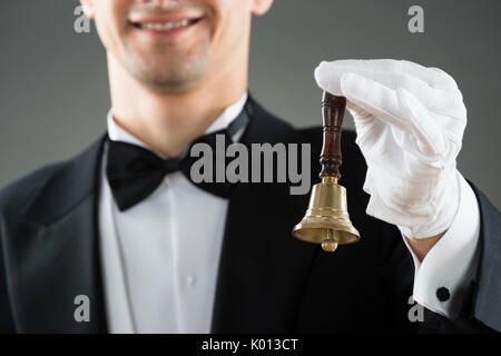 Midsection of waiter holding ring bell against gray background Stock Photo