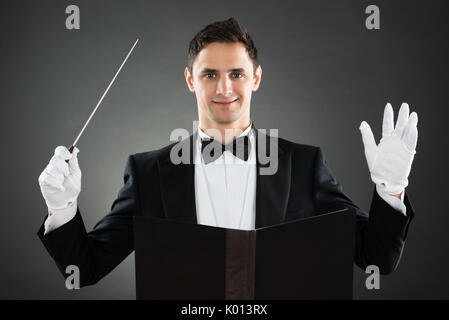 Portrait of smiling music conductor holding baton against gray background Stock Photo