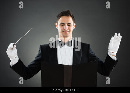 Portrait of smiling music conductor holding baton against gray background Stock Photo