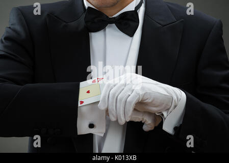 Midsection of magician performing magic trick with cards against gray background Stock Photo