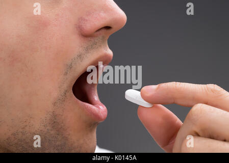 Cropped image of man taking medicine against gray background Stock Photo