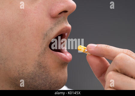 Cropped image of man taking medicine against gray background Stock Photo