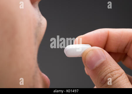 Cropped image of sick man taking medicine against gray background Stock Photo