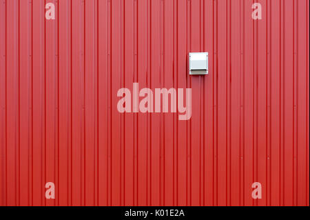 Red tin wall with vertical lines and beige exhaust vent Stock Photo