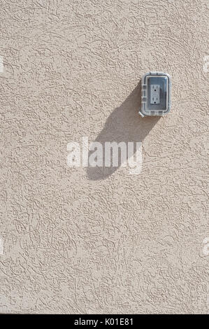 Covered electrical socket casts a shadow on textured wall Stock Photo