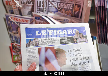 LONDON, ENGLAND - MAY 14, 2017 : A hand holding Le Figaro newspaper over newsstand background in Paris. Le Figaro is a French daily morning newspaper  Stock Photo