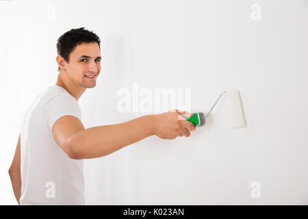 Young man using paint roller on white wall at home Stock Photo