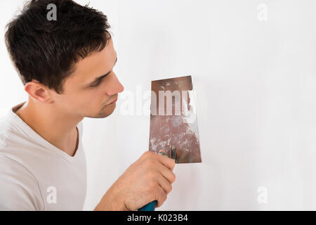 Young man using putty knife on white wall at home Stock Photo
