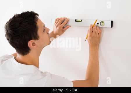 Rear view of young man using spirit level on white wall at home Stock Photo