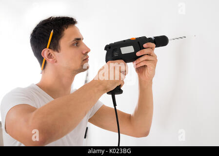 Young man using power drill on white wall at home Stock Photo