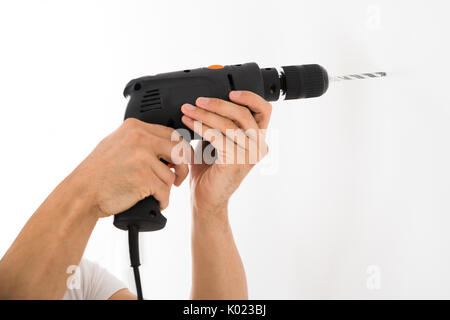 Cropped image of young man using power drill on white wall at home Stock Photo