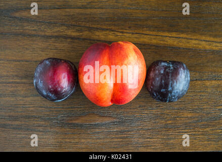 plums and a peach on wooden table viewed from above Stock Photo