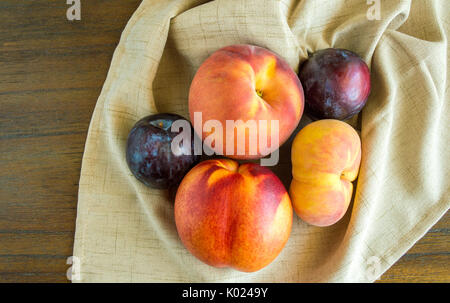 group of plums and peaches in a beige napkin on a wooden table viewed from above Stock Photo