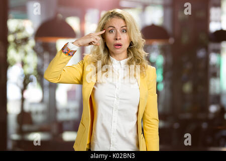 Shocked young woman touching her forehead. Surprised attractive business woman recollected something, blurred background. Stock Photo