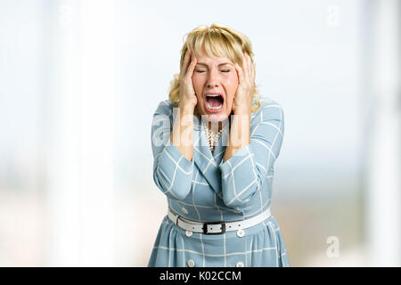 Mature woman screaming in despair. Close up shot of stressed and shocked white-skin woman screaming with desperate and horrified expression, hands on  Stock Photo