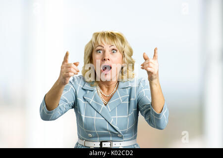 Surprise astonished mature woman. Close up portrait of middle aged woman looking surprised and having an idea with wide open mouth and raised hands. Stock Photo