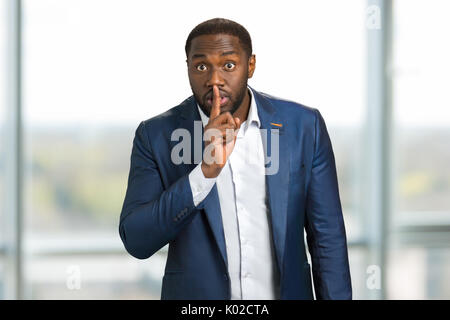 Businessman holding index finger on lips. Black man showing silence gesture with finger on his lips. Sign keep a silence. Stock Photo