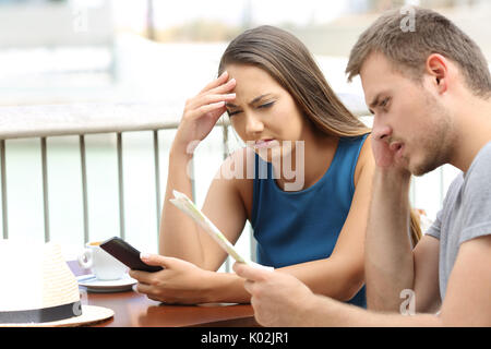 Two confused tourists reading a map outdoors sitting in a coffee shop Stock Photo