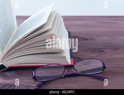 Open book and glasses lying on a wooden background with toning. Stock Photo