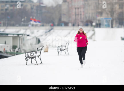 Pretty girl wearing sportswear and running on snow during winter Stock Photo