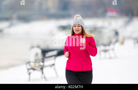 Pretty girl wearing sportswear and running on snow during winter Stock Photo