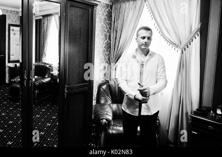 Portrait of a stunning groom dressing up for the wedding and getting ready in his room. Black and white photo. Stock Photo