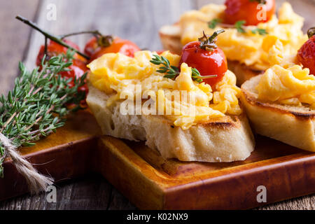 Bruschetta with scrambled eggs and oven roasted cherry tomatoes, delicious summer appetizer Stock Photo
