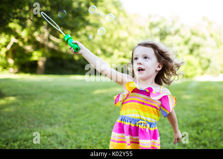 Preschool girl playing with bubble wand in summer yard Stock Photo
