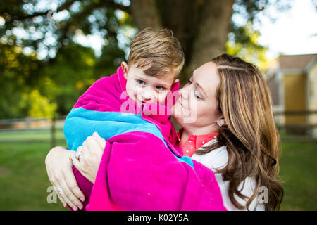 Affectionate mother holding son wrapped in a towel in summer yard Stock Photo