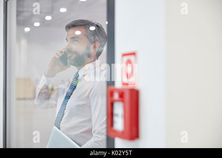 Male supervisor talking on cell phone at window in factory Stock Photo