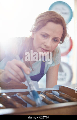 Focused female painter painting furniture with blue paint Stock Photo