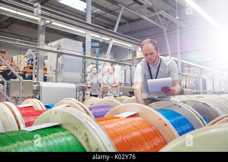 Male worker with clipboard checking multicolor spools in fiber optics factory Stock Photo