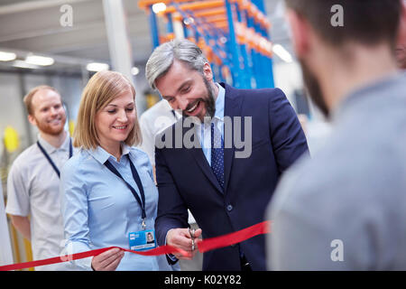 Businessman and businesswoman cutting ceremonial ribbon in fiber optics factory Stock Photo