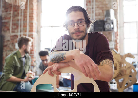 Portrait confident male designer with tattoos leaning on prototype in workshop Stock Photo