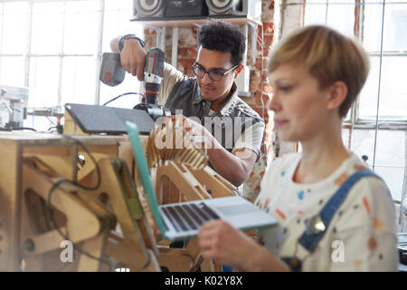 Designers using laptop and power drill in workshop Stock Photo