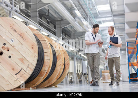 Male supervisor and worker with clipboard walking in fiber optics factory Stock Photo