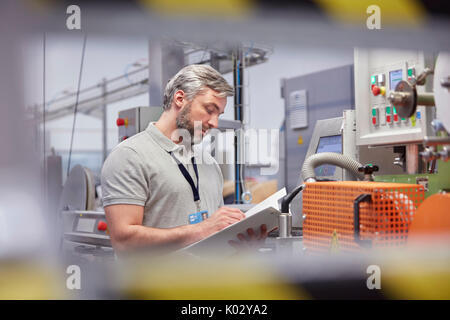 Male supervisor with clipboard at machinery control panel in fiber optics factory Stock Photo