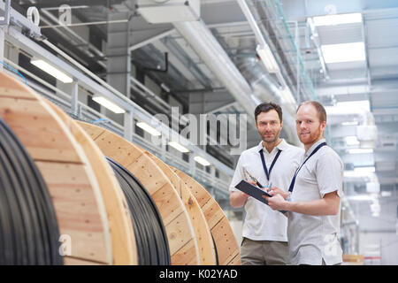 Portrait smiling male supervisors with clipboard talking in fiber optics factory Stock Photo