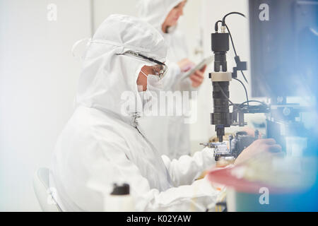 Workers in protective suits using machinery in fiber optics research and testing laboratory Stock Photo