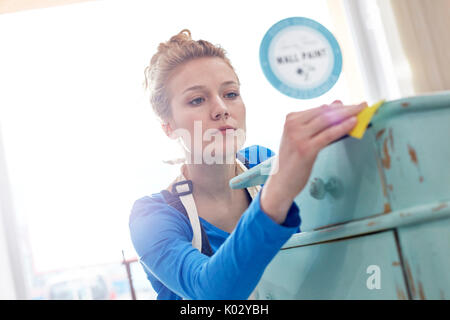 Focused young female artist sanding side table in art studio Stock Photo