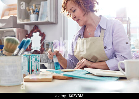 Mature female artist painting picture frames in art studio Stock Photo