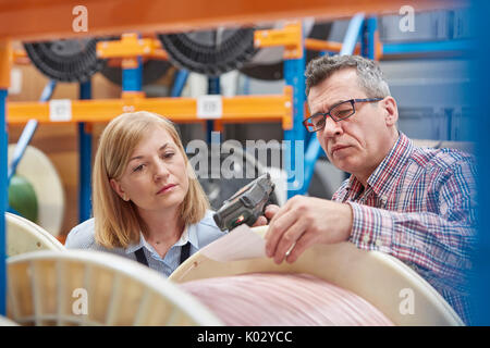 Male and female supervisors using IR code scanner, scanning spool in fiber optic warehouse Stock Photo