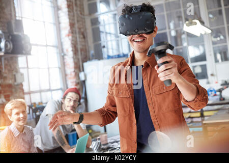 Smiling male computer programmer texting virtual reality simulator glasses and joystick in workshop Stock Photo