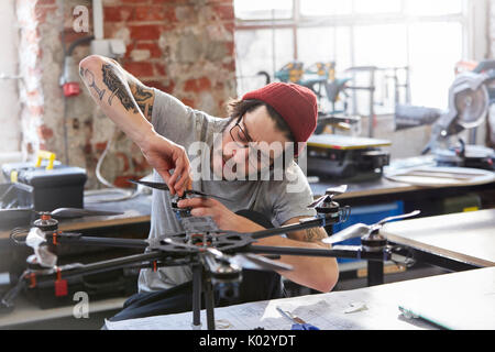 Male designer with tattoos assembling drone in workshop Stock Photo