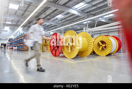 Male worker walking by large spools in fiber optics factory Stock Photo